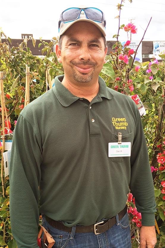 A man in a green shirt standing in front of flowers.