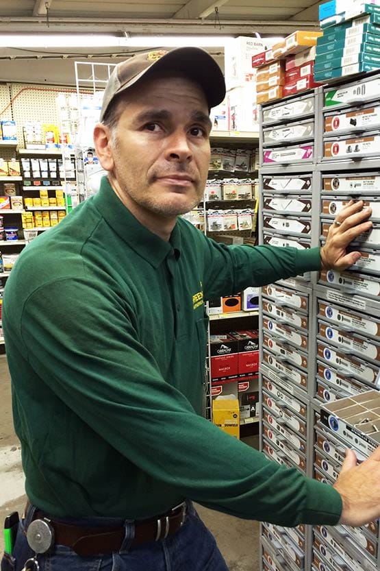 A man in a green shirt standing next to a rack of cigarettes.