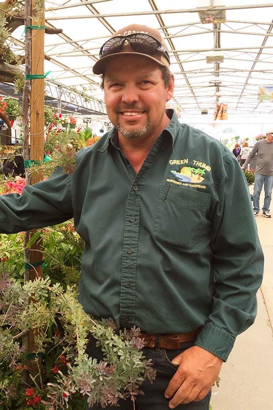 A man standing next to a plant in a greenhouse.