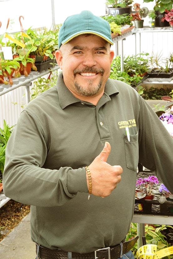 A man giving a thumbs up in a greenhouse.