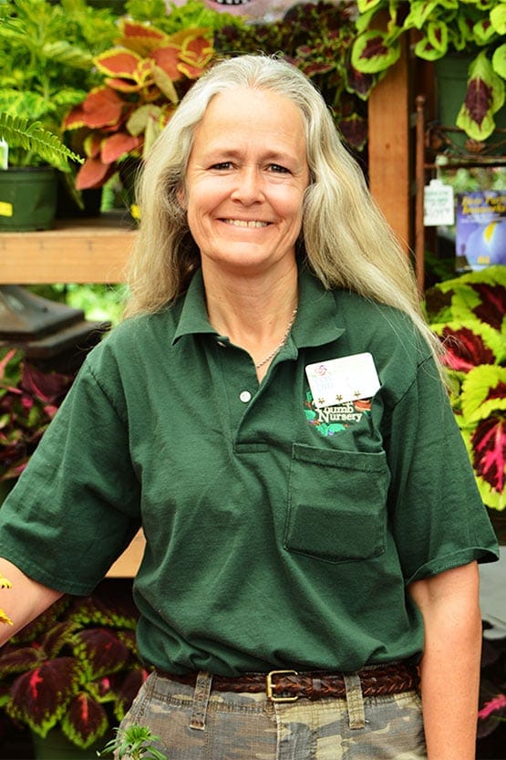 A woman in a green shirt standing in front of plants.