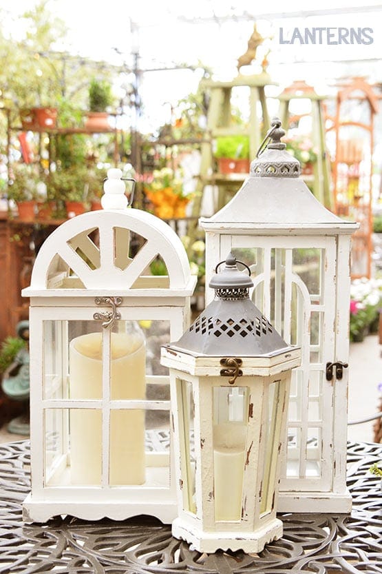 Three white lanterns sitting on a table in a garden.