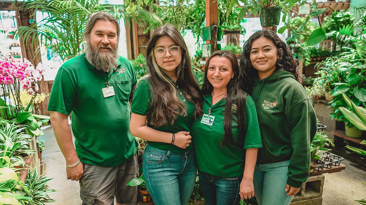 A group of people in green shirts standing in front of plants at the best plant nursery near me.