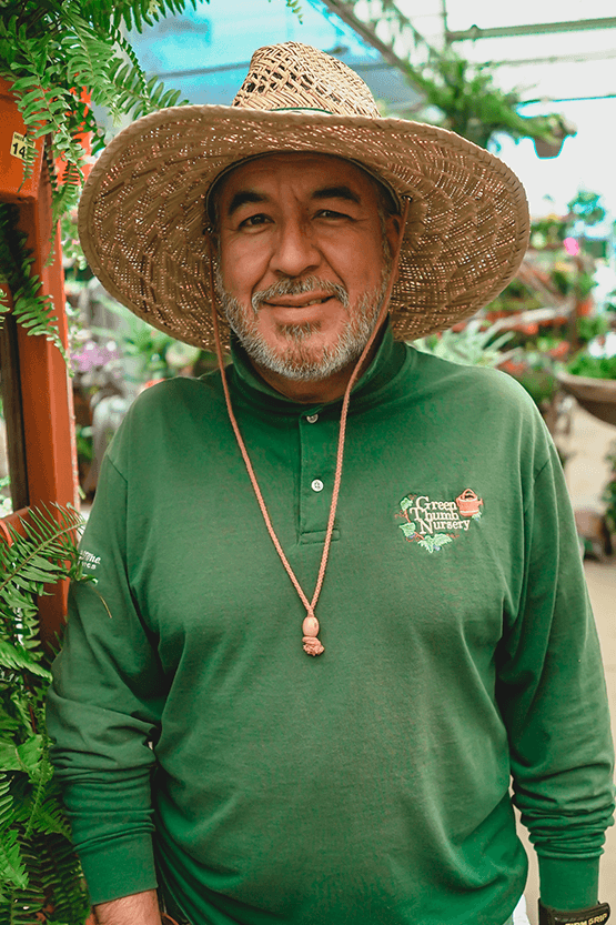 A man in a straw hat tending to plants in a greenhouse at the best plant nursery near me.