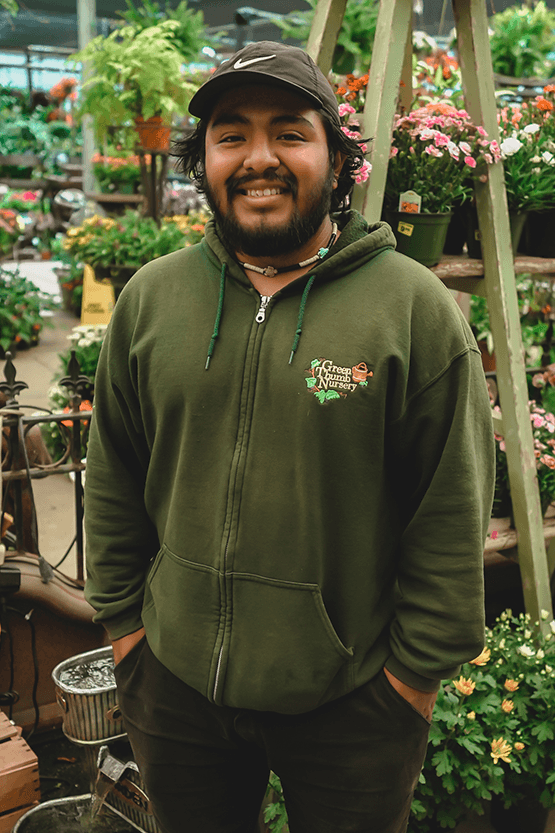 A man in a green hoodie browsing plants at a nursery.