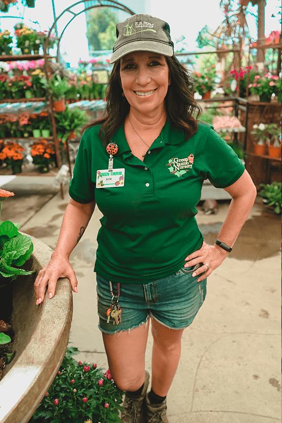 A woman in a green shirt standing in a garden center near me.