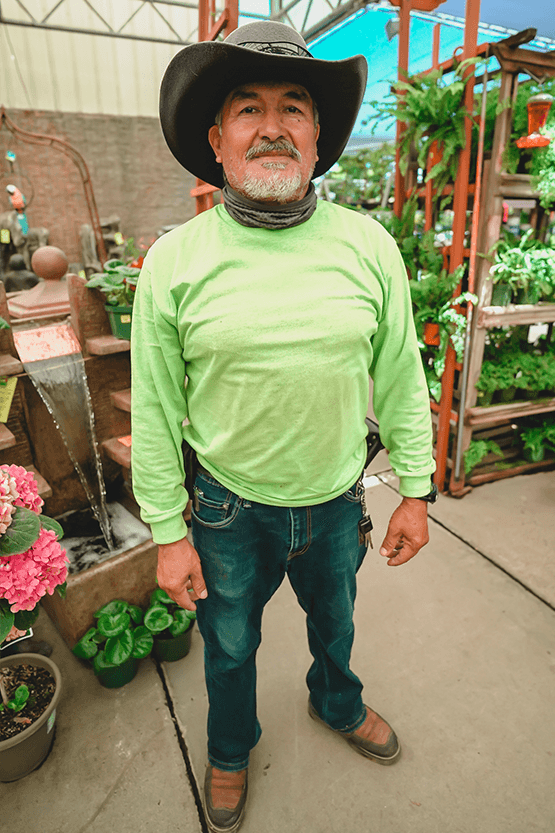 A man in a cowboy hat standing in a plant nursery.