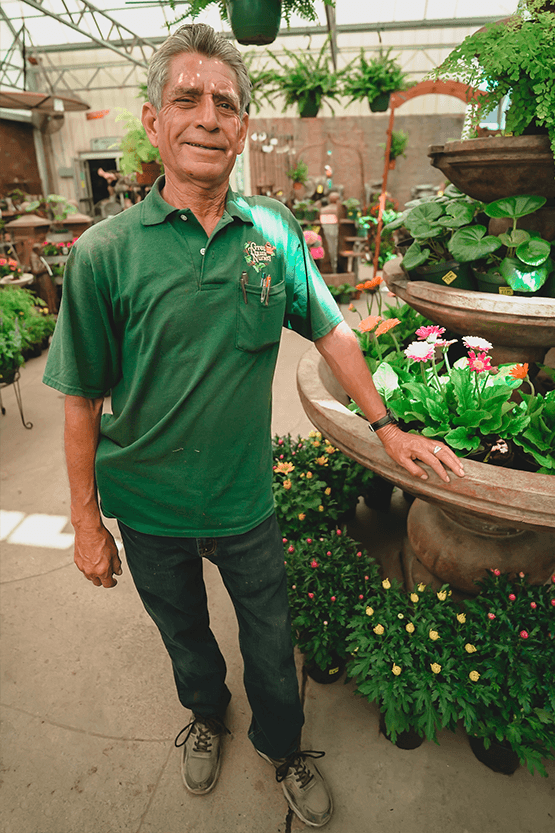 A man standing in front of a plant nursery full of plants.