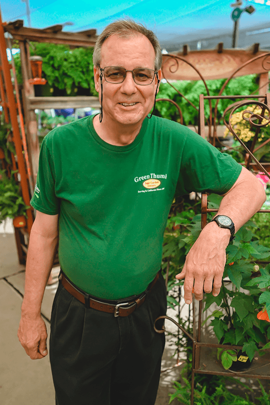 A man in a green shirt standing in front of plants at a nursery near me.