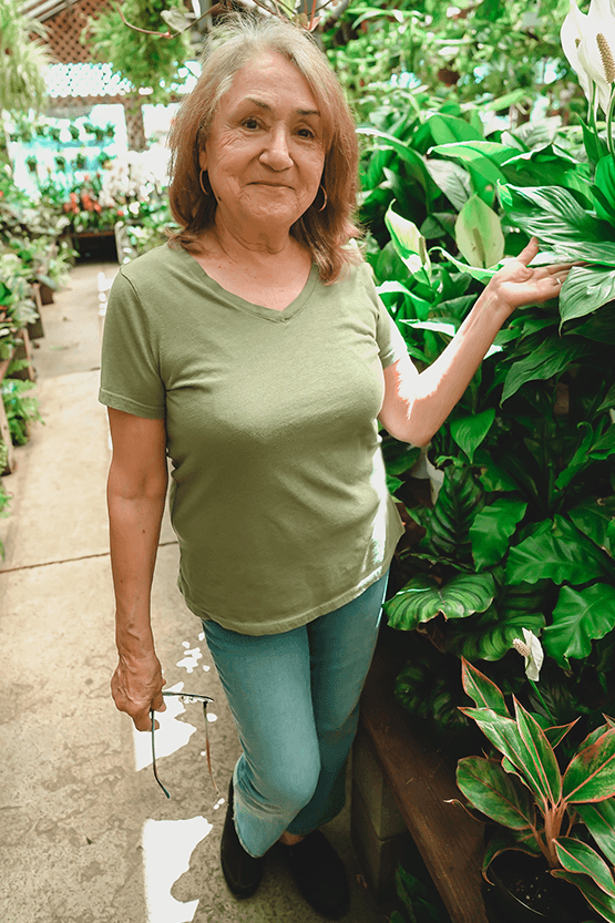 A woman standing in a greenhouse wearing a green shirt, showcasing the best nursery near me.