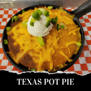 A cast iron skillet filled with cornbread topped with melted cheddar cheese, sour cream, and chopped green onions, on a red and white checkered paper. Text reads "Texas Pot Pie.