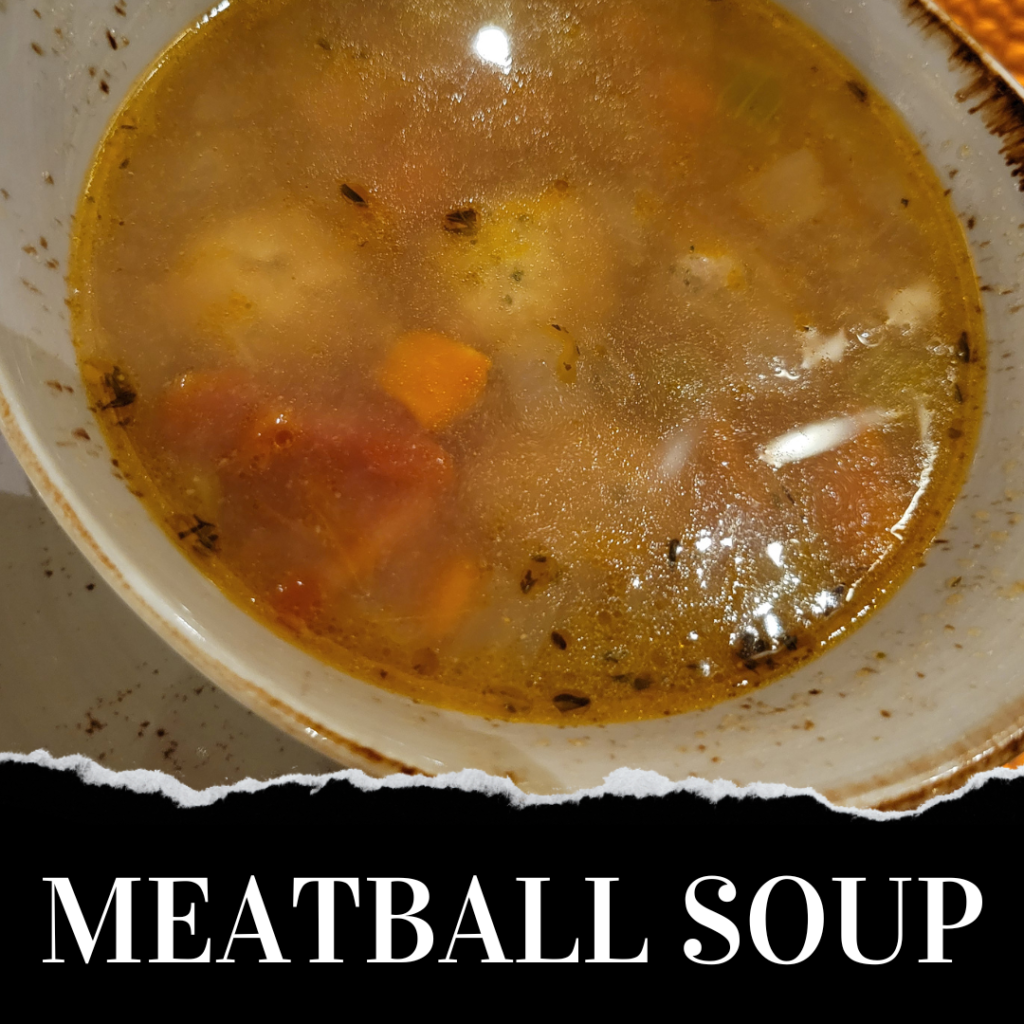 A bowl of meatball soup with carrots and herbs.