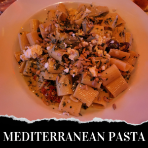 A plate of Mediterranean pasta topped with herbs, cheese, and seeds. Text at the bottom of the image reads "MEDITERRANEAN PASTA.