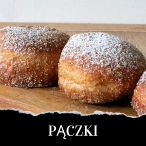 Three powdered sugar-covered Polish doughnuts, known as pączki, are displayed on a wooden surface.