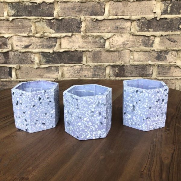 Three hexagonal terrazzo planters with a blue and white pattern are arranged on a wooden table with a brick wall in the background.