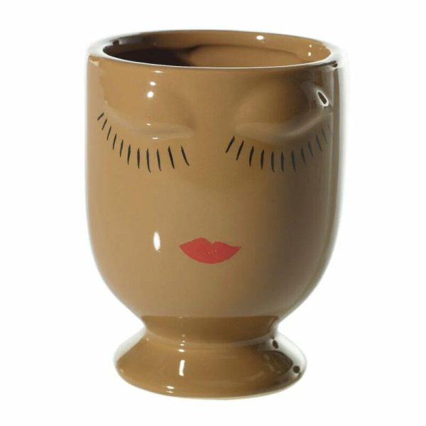 A brown ceramic cup with a closed-eye face design and red lips painted on the front.