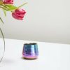 A small iridescent candle holder sits on a reflective surface next to partially visible pink tulips.